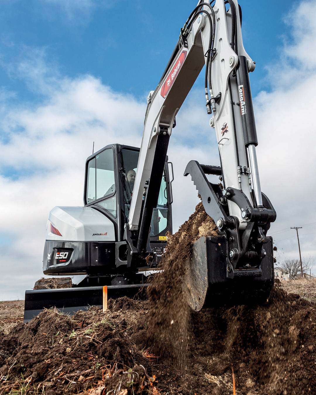 This image features a Bobcat E50 mini excavator in action at a job site, utilising its long arm attachment to dig and move soil efficiently. The machine's compact yet powerful design allows it to handle heavy-duty digging and earthmoving tasks with precision. The operator is working on site preparation, highlighting the excavator's capability to perform in various environments. The E50 model is well-suited for both commercial and residential projects where tight manoeuvrability and strength are required for excavation work.
