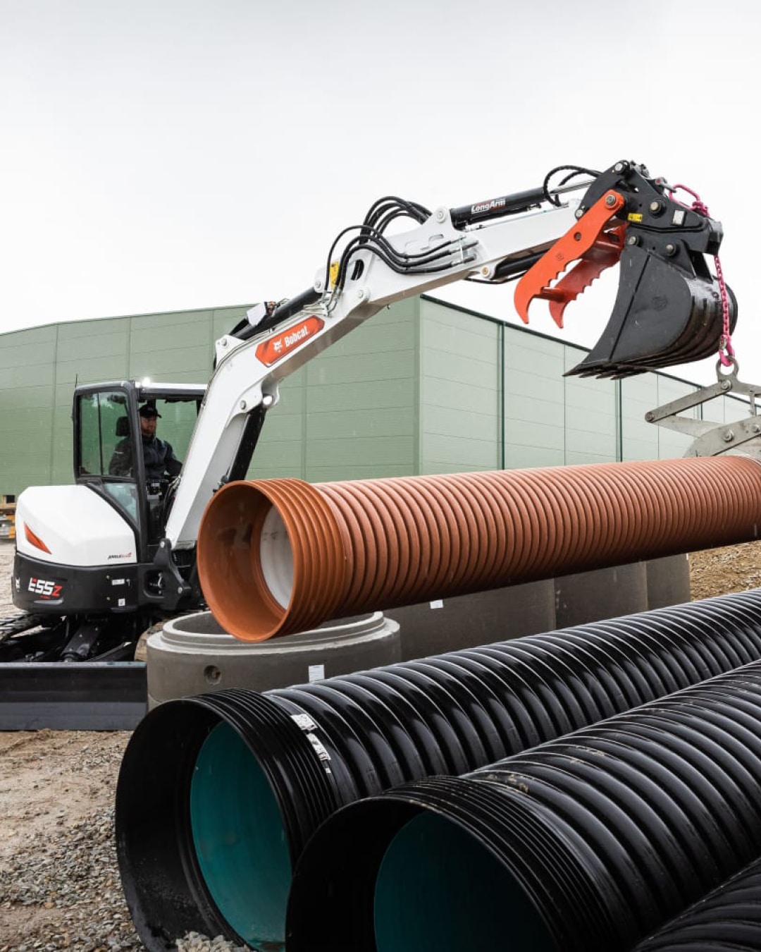 The Bobcat E55z Mini Excavator demonstrates its versatility by precisely manoeuvring large drainage pipes, showcasing its superior lifting and placement capabilities for infrastructure projects.