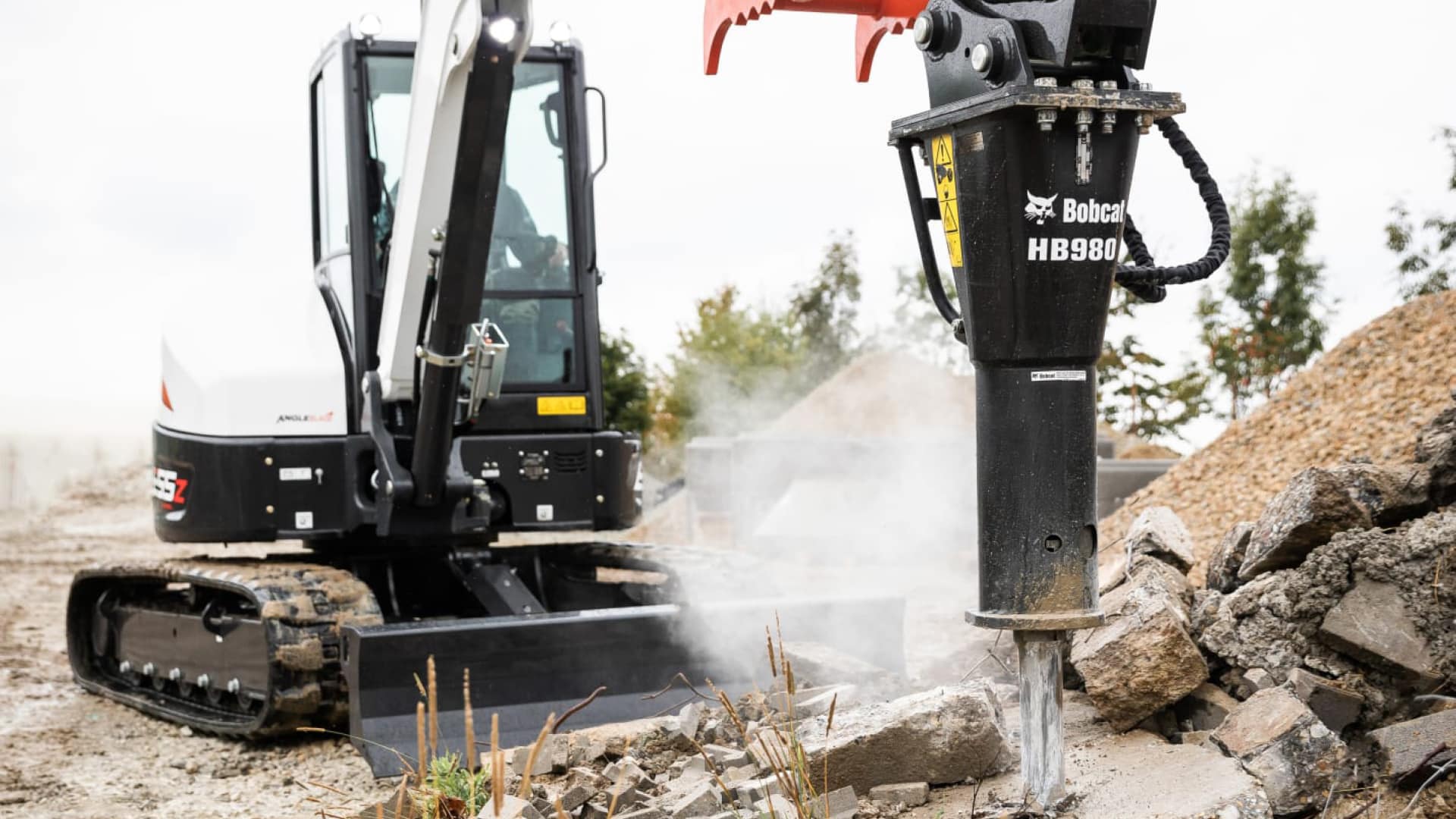 The Bobcat E55z Mini Excavator utilises a HB980 hydraulic breaker attachment to efficiently break down concrete rubble on a construction site. The compact yet powerful machine demonstrates its versatility and strength in handling tough demolition tasks with ease.