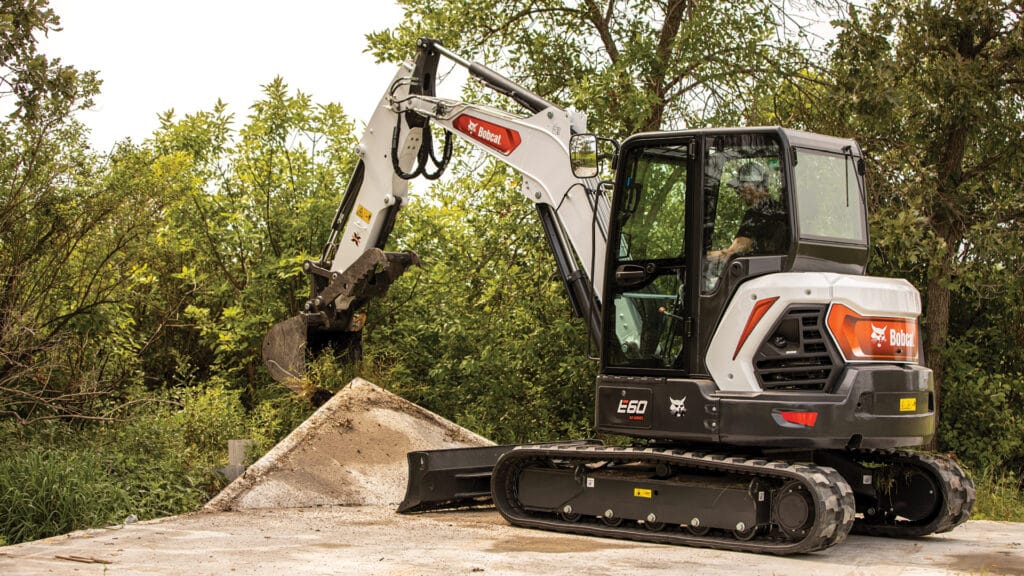 The Bobcat E60 Mini Excavator operating in a woodland setting, skilfully handling concrete debris, showcases its adaptability and precision for diverse terrains.