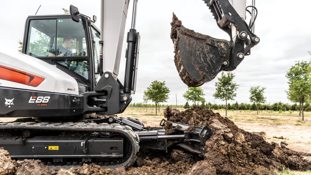 A Bobcat E88 Mini Excavator at work, showcasing its precision digging capabilities and the robust R2-Series design, ideal for landscaping and agricultural applications.