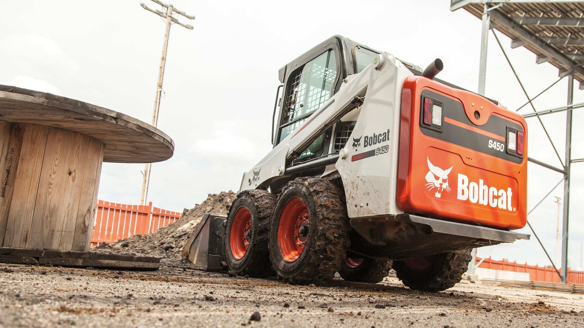 A Bobcat Skid Steer Loader on a construction site, equipped with a bucket attachment, handling dirt and debris with ease, while surrounded by industrial materials and equipment in an outdoor setting.