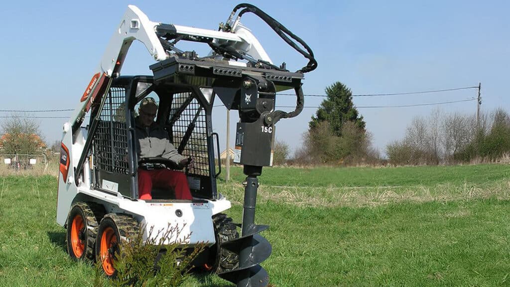Bobcat S100 Skid Steer Loader equipped with a powerful auger attachment, efficiently drilling into the ground in a grassy field, showcasing its versatility and precision in landscaping and agriculture applications.