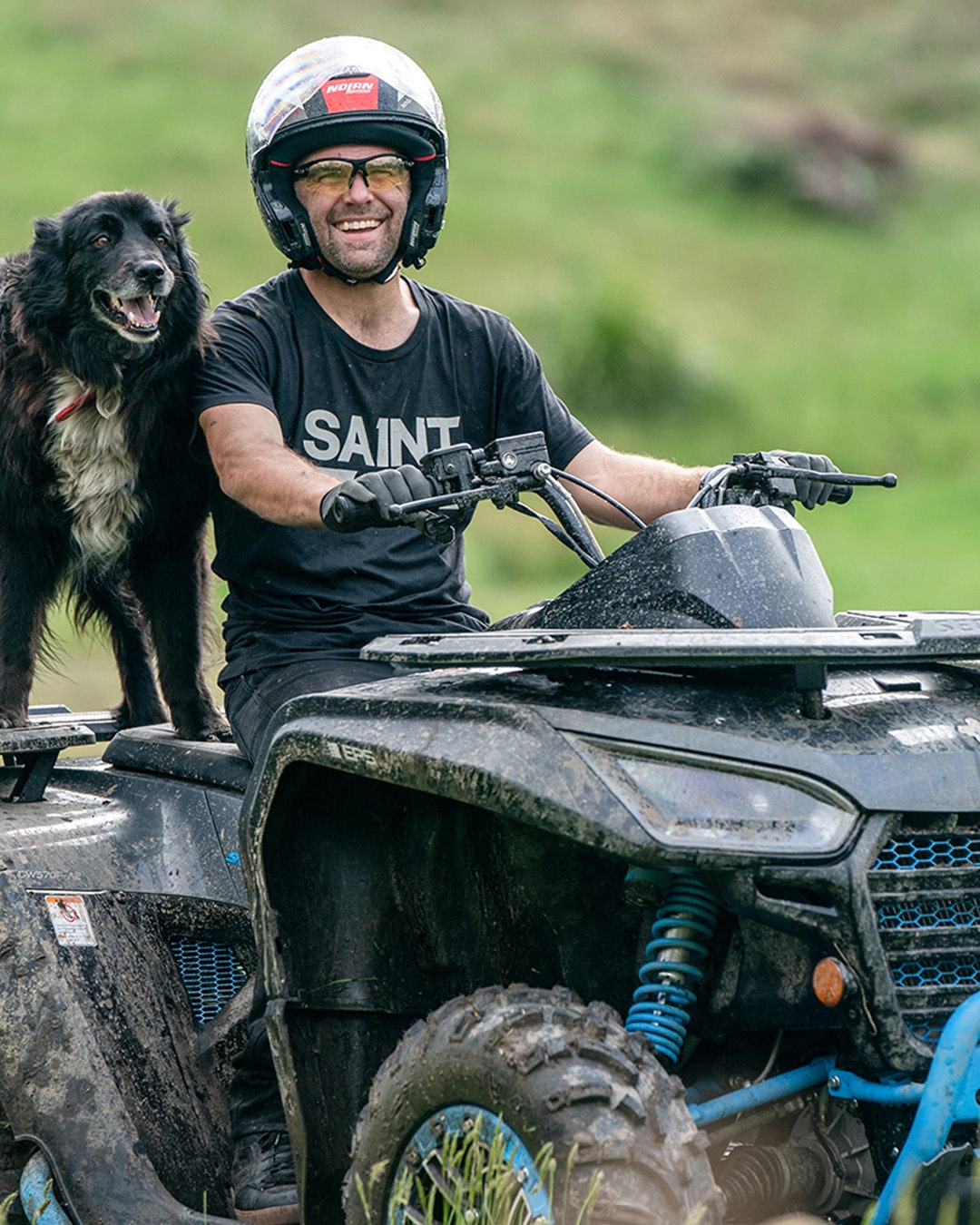 A smiling rider wearing a helmet and sunglasses sits on a muddy Segway Farm Quad Bike with a happy farm dog standing beside him, showcasing the bike’s durability and suitability for working alongside loyal companions in rural settings.