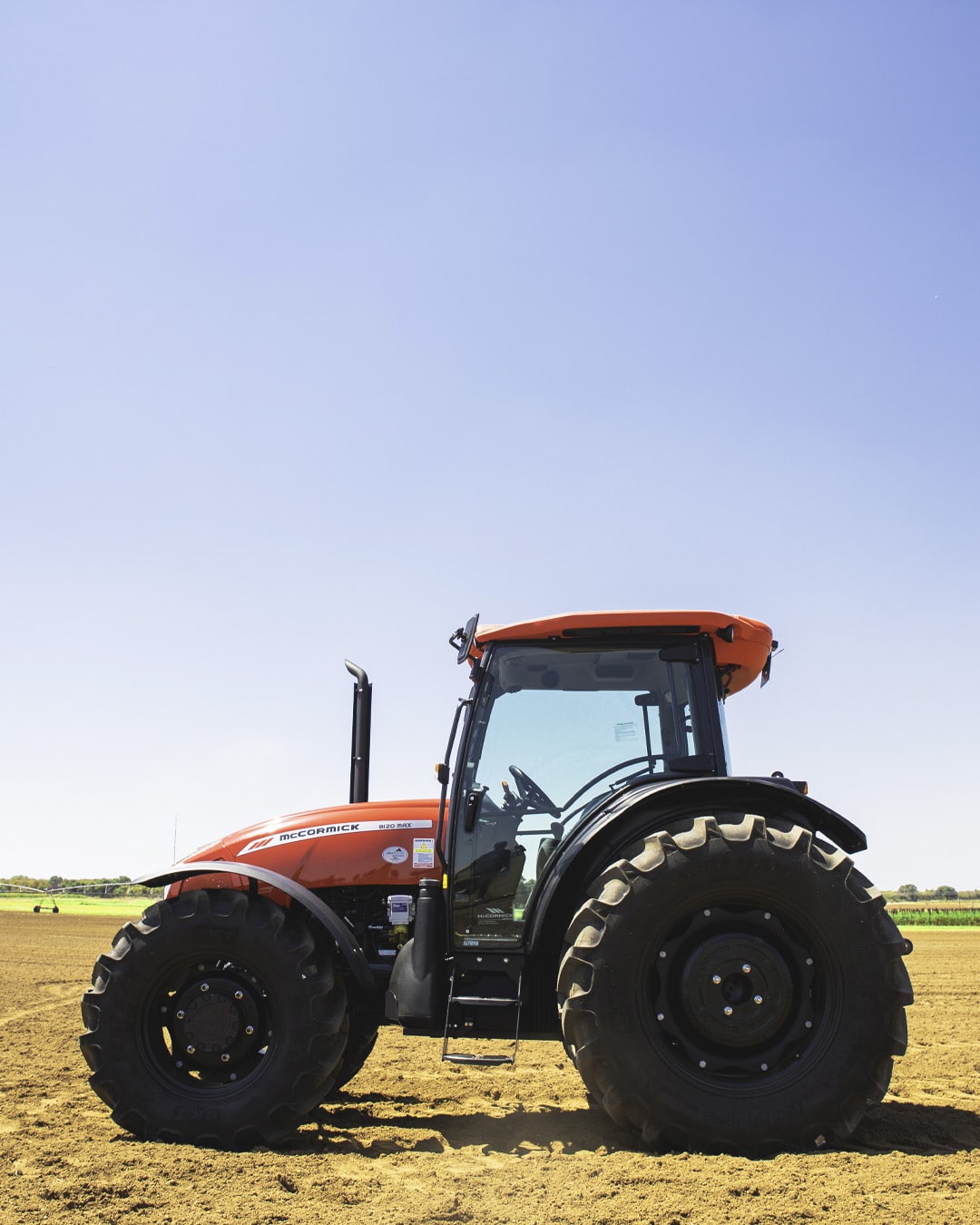McCormick B-MAX Farm Tractor side profile on a cultivated field, featuring large rear tyres, enclosed cab, and a clear blue sky in the background.