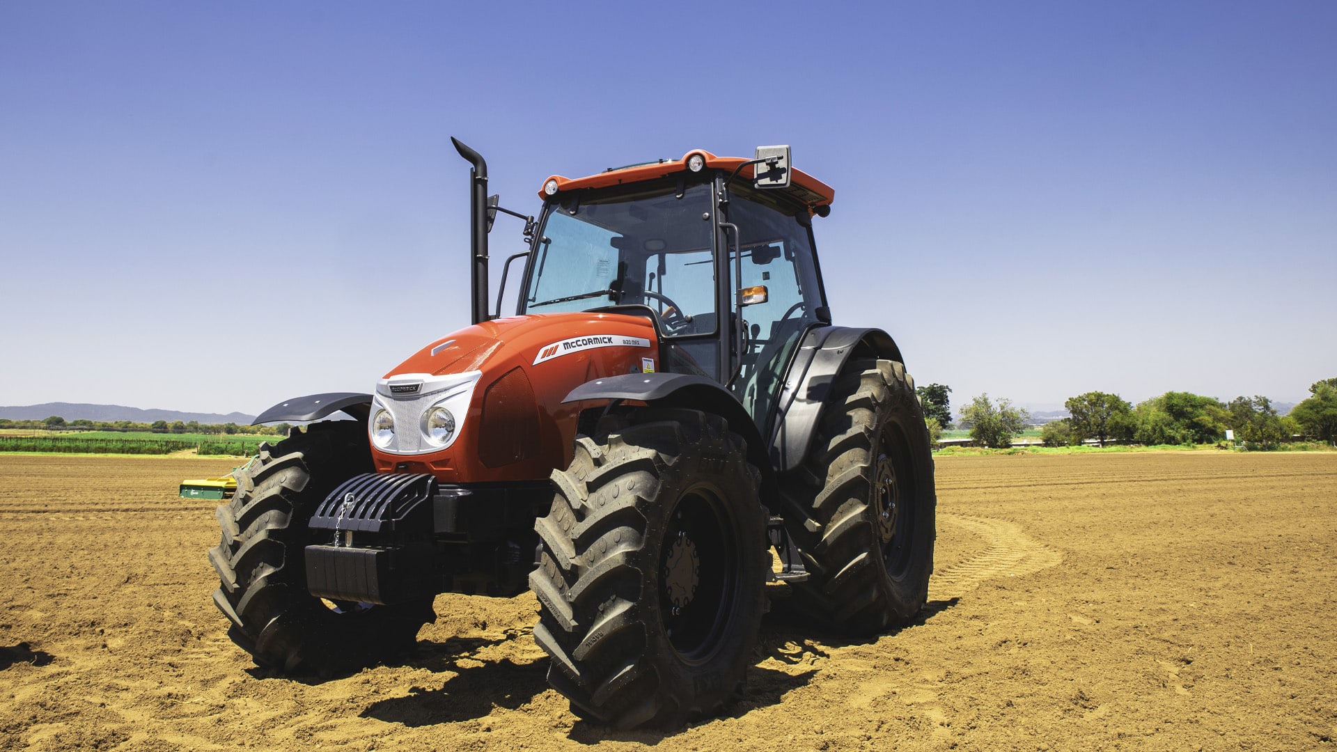 McCormick B-MAX Farm Tractor parked on a freshly tilled field under a clear blue sky, showcasing its rugged build and wide agricultural tyres.