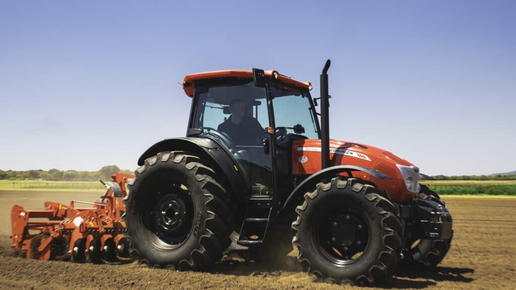 McCormick B-MAX Farm Tractor cultivating a freshly tilled field with rear disc harrow attachment on a sunny day.