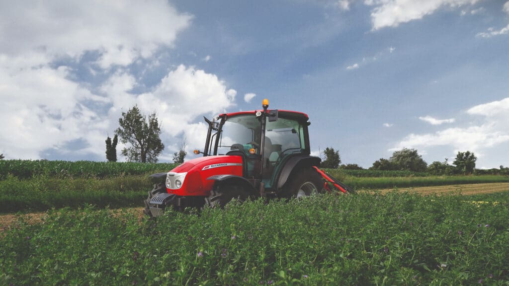 McCormick X5 Farm Tractor operating on a lush green hillside under a partly cloudy sky, demonstrating its versatility in row crop and pasture work.