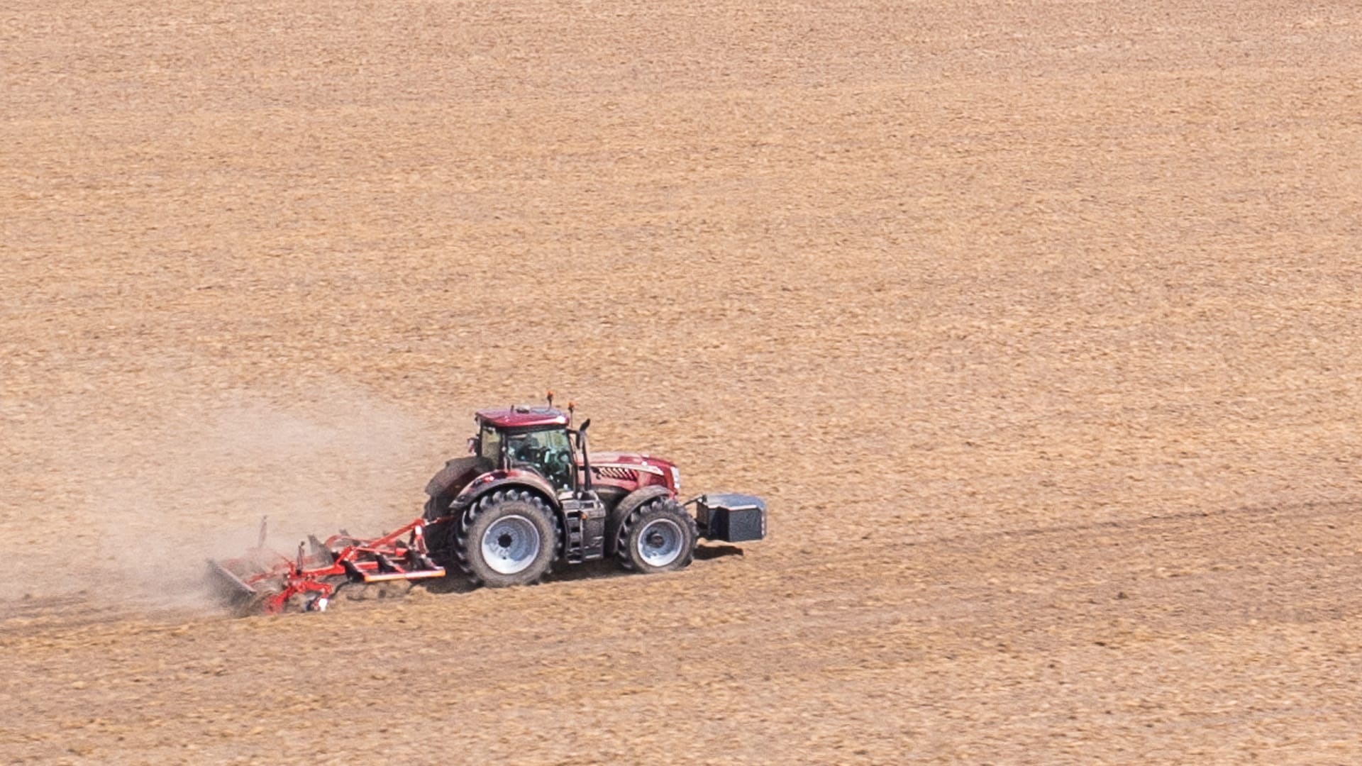 McCormick X8 Farm Tractor captured mid-field from a distance, pulling a wide cultivator across dry, open farmland, showcasing its power and efficiency in broadacre operations.