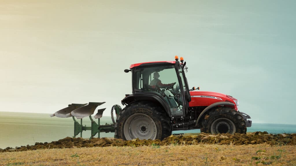 McCormick tractor ploughing a hillside paddock near the coastline at sunrise.