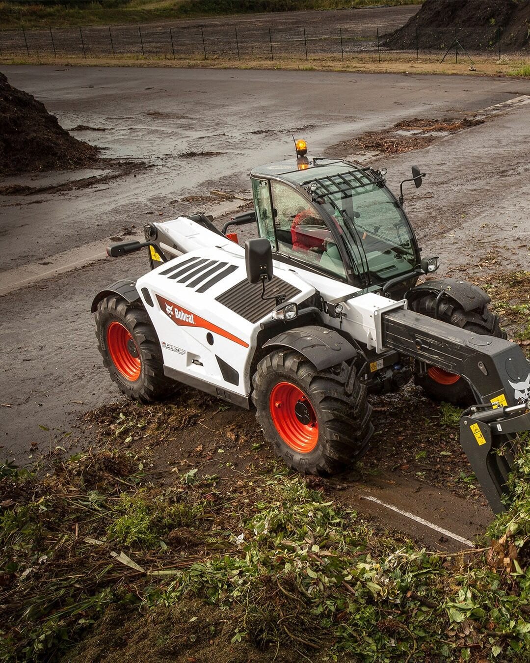 A Bobcat Agricultural Telehandler working on a green waste site, gathering plant debris with a grapple attachment after recent rainfall.