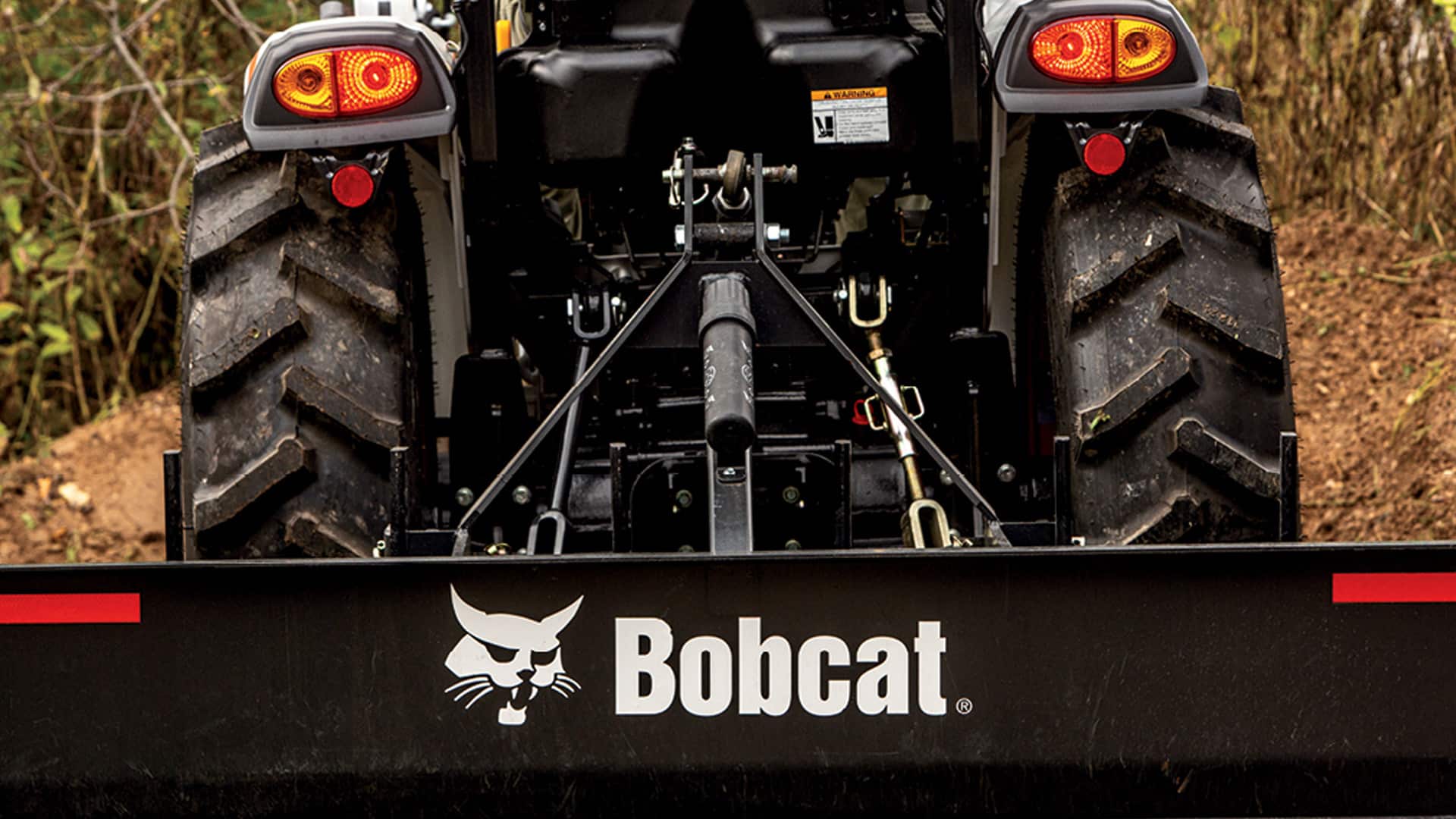 Rear view of a Bobcat CT2035 Compact Tractor connected to a rear blade attachment, showcasing its durable build, large agricultural tires, and versatile three-point hitch system.