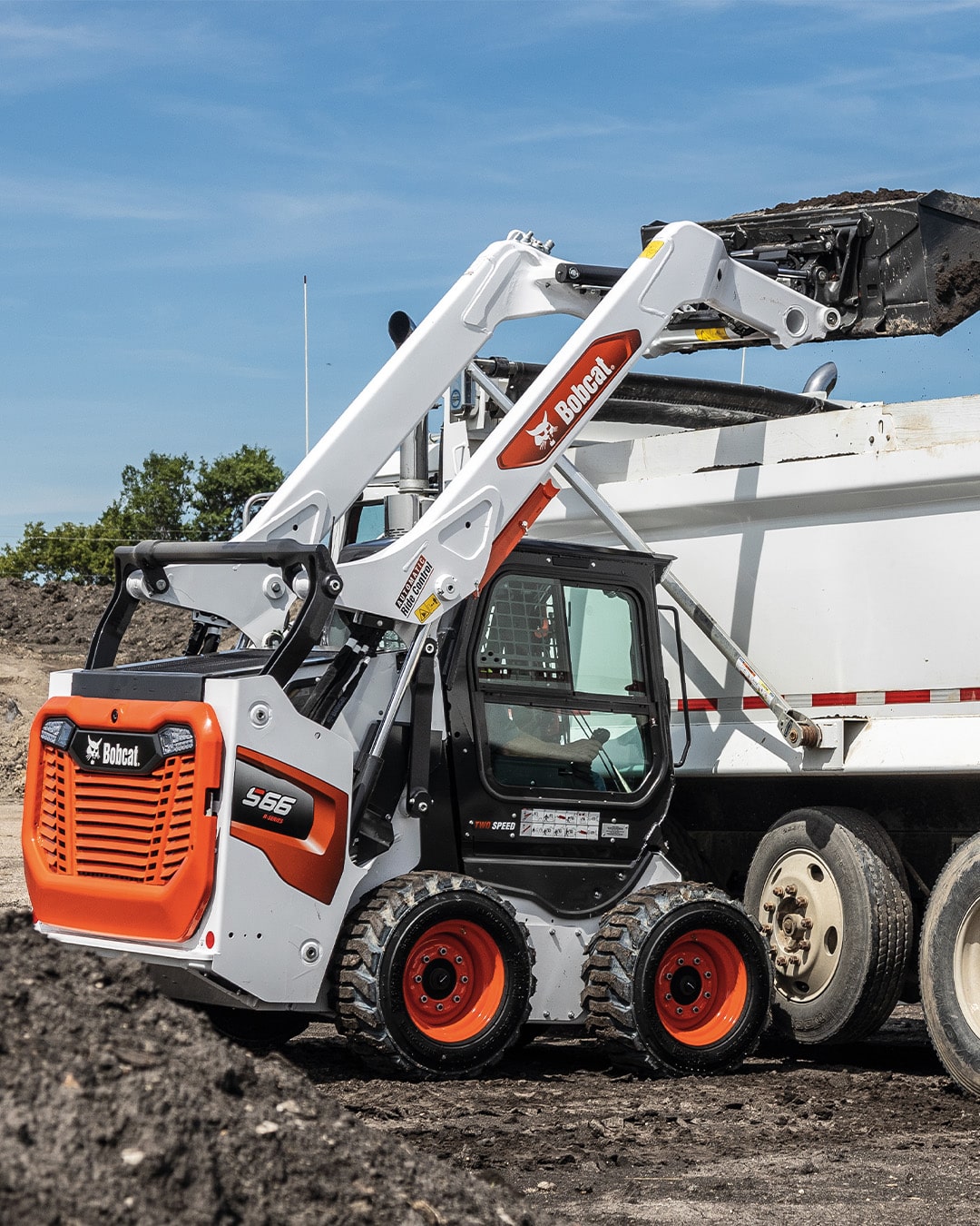 Bobcat S66 Skid Steer Loader loading dirt into a dump truck, showcasing powerful lift capabilities and efficient material handling.