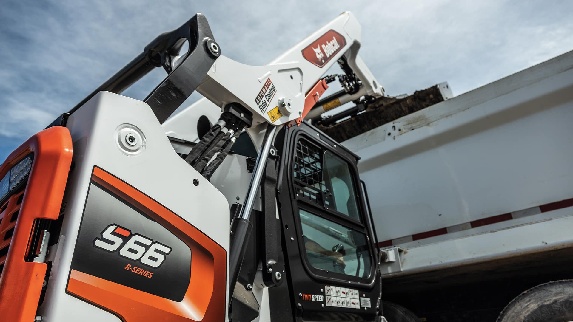 Bobcat S66 Skid Steer Loader unloading dirt into a dump truck, highlighting its efficient load-handling capabilities and robust R-Series design.