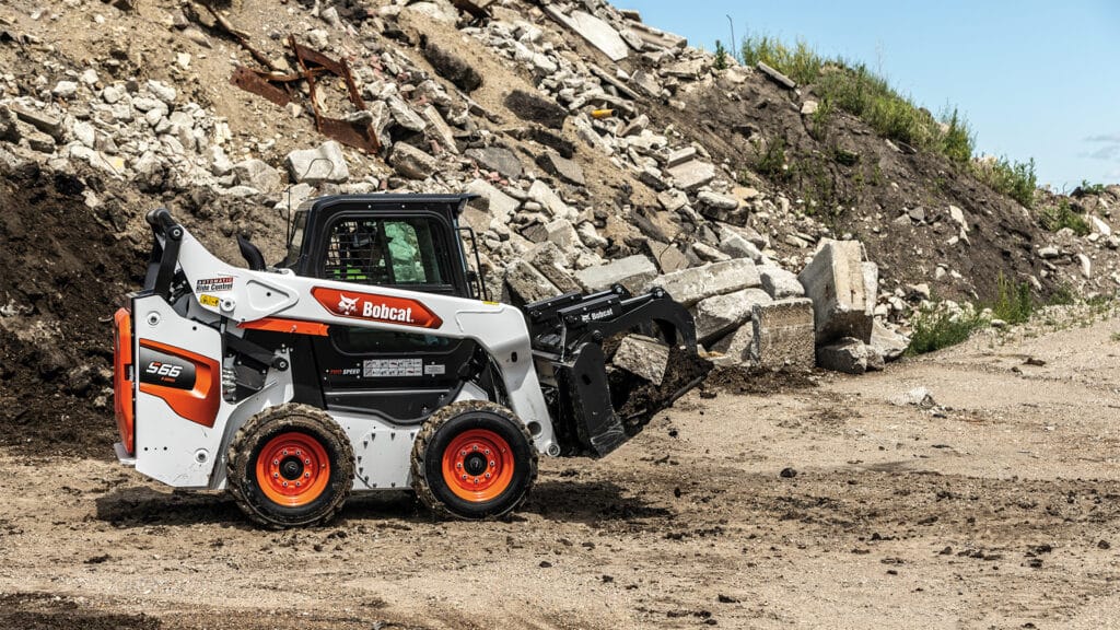 Bobcat S66 Skid Steer Loader manoeuvring through a construction site with a grapple attachment, showcasing its power and versatility in handling heavy debris.
