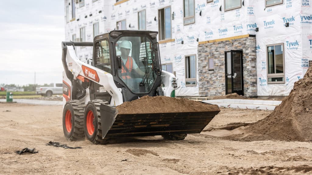 Bobcat S76 Skid Steer Loader moving a full bucket of soil on a construction site, delivering efficient material handling and precise control.