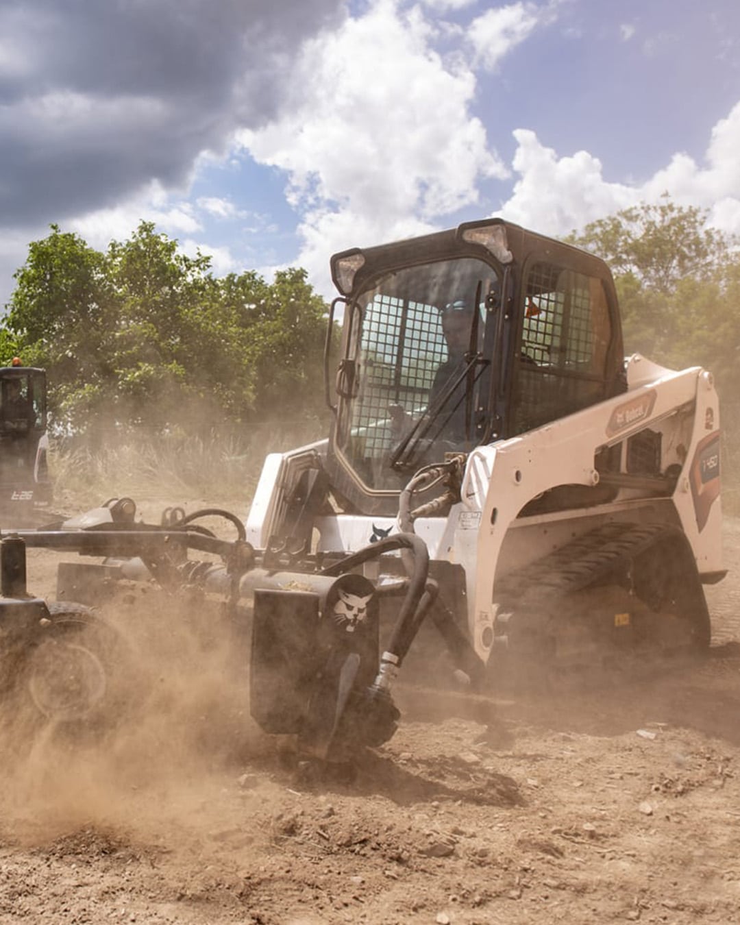 Bobcat T450 Track Loader equipped with a soil conditioner attachment, working efficiently on dusty terrain under a partly cloudy sky.