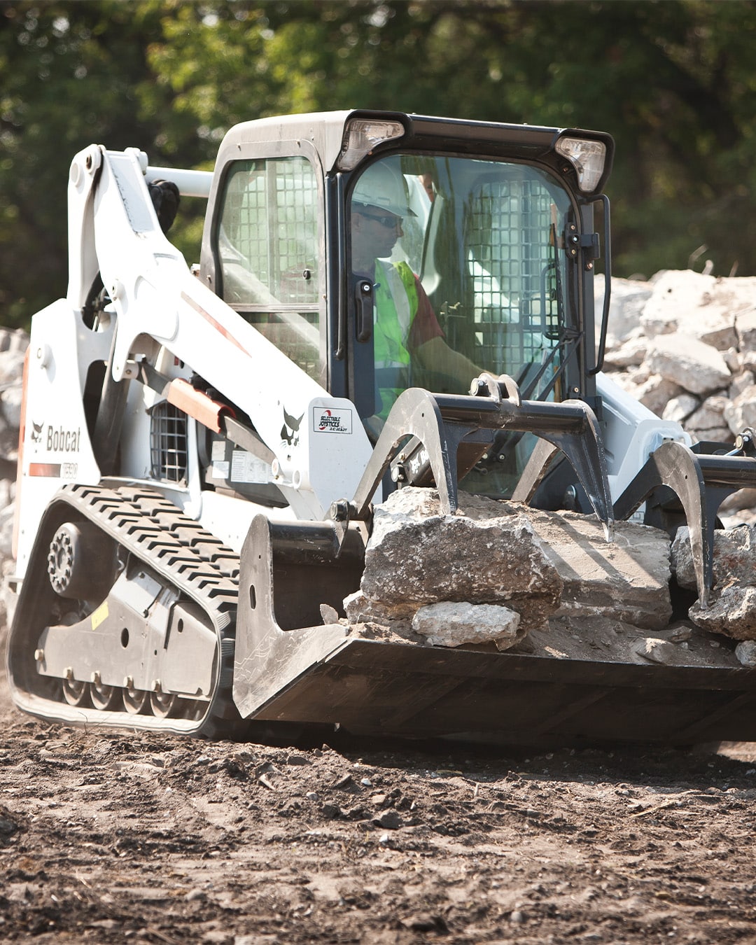 Bobcat T590 Track Loader transporting large chunks of concrete rubble with a grapple bucket on a rugged construction site.