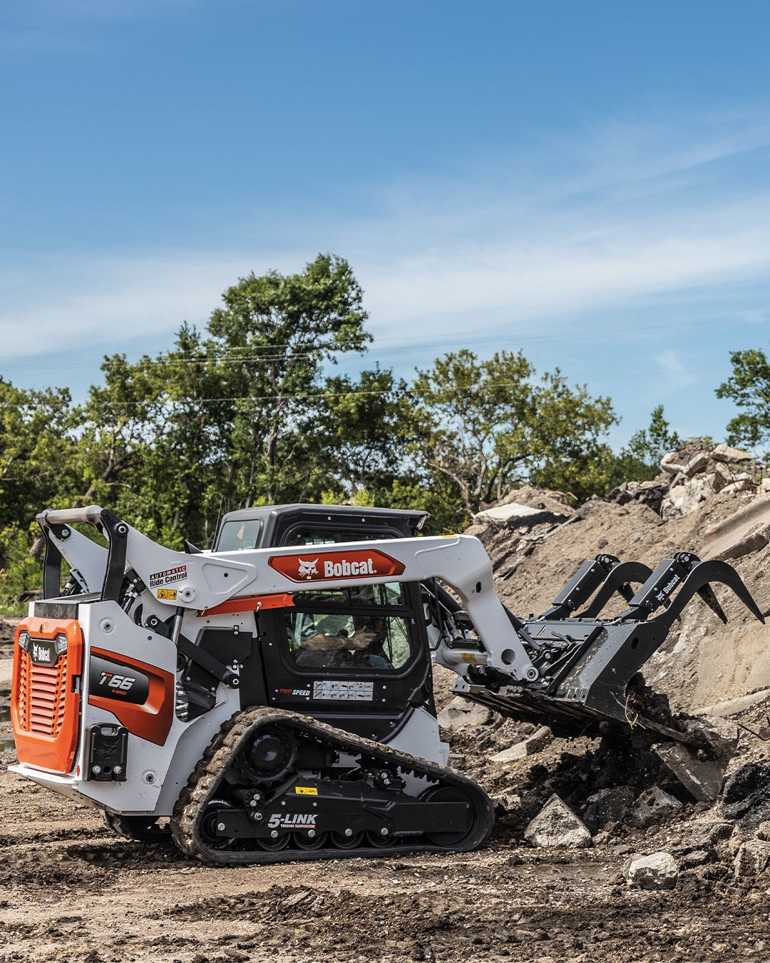 Bobcat T66 Track Loader using a grapple attachment to move large rocks and debris, showcasing robust handling and material clearing capabilities on rugged terrain.