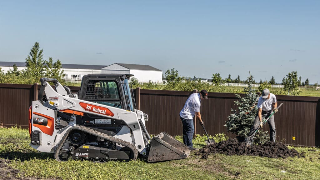 A Bobcat T66 Track Loader assisting with landscaping as two workers plant a tree, showcasing efficient earthmoving and material handling capabilities.