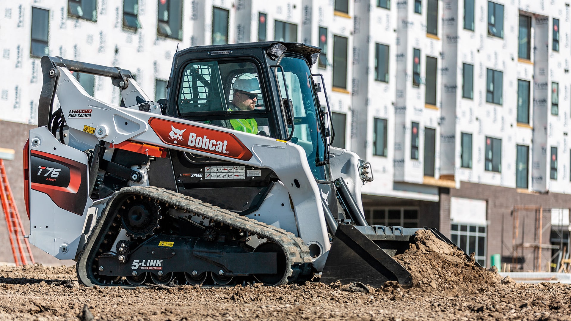 A Bobcat T76 Track Loader with operator levelling dirt on a construction site, demonstrating precision and control for grading tasks.