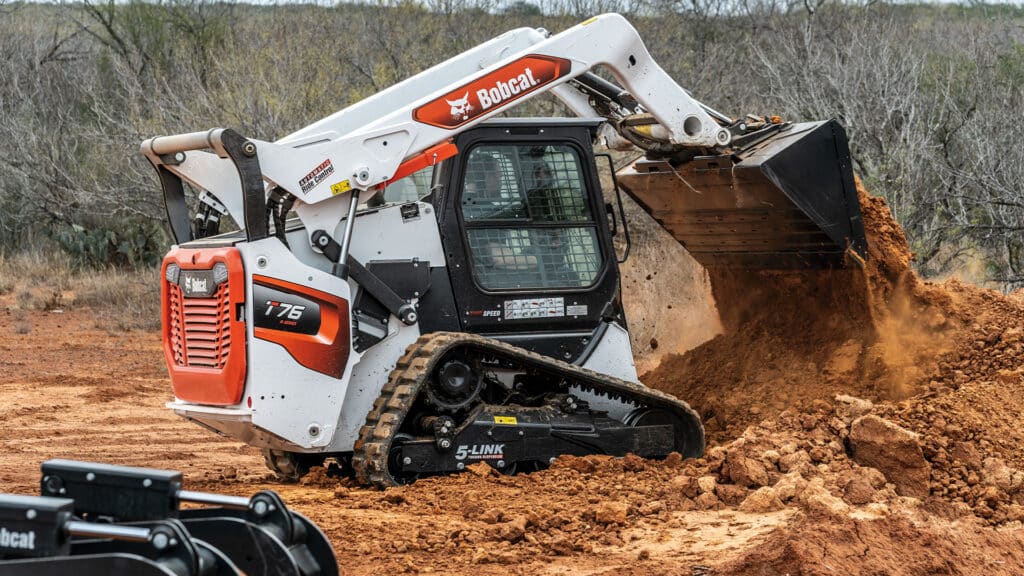 A Bobcat T76 Track Loader dumping a load of dirt on a rugged job site, showcasing powerful performance and efficiency in earthmoving tasks.