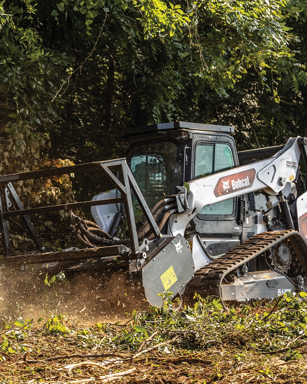 A Bobcat T86 Track Loader clearing dense vegetation with a forestry cutter attachment, demonstrating its powerful performance and rugged capability in challenging terrain.