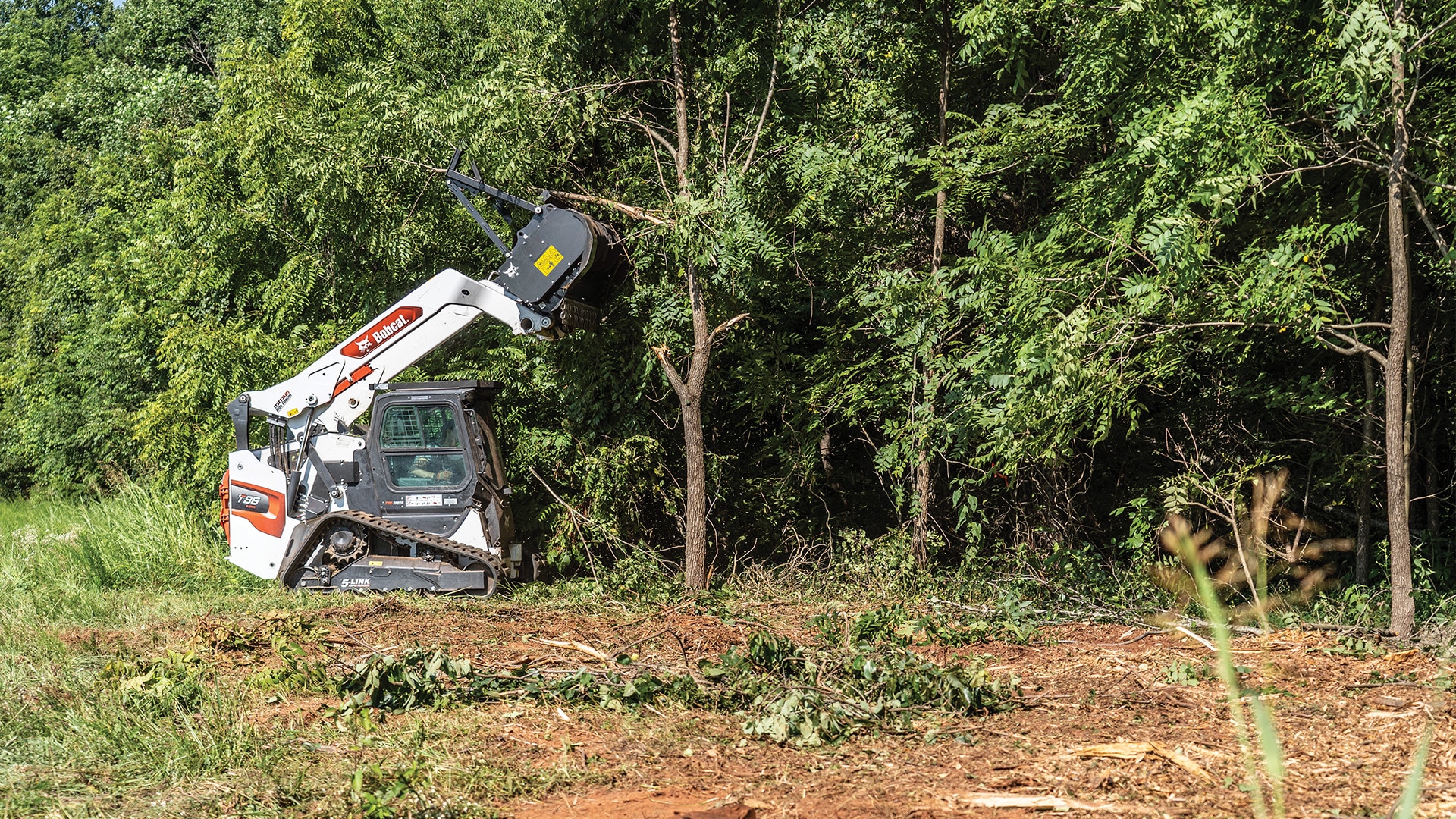 A Bobcat T86 Track Loader using a forestry cutter attachment to trim tree branches, showcasing its versatility and strength in vegetation management.