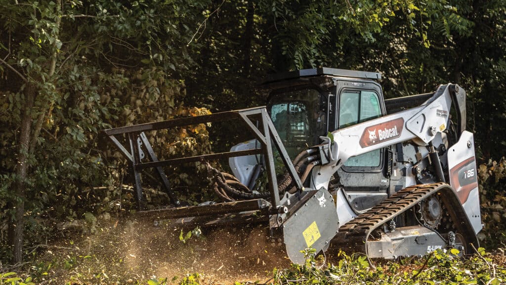 A Bobcat T86 Track Loader clearing dense vegetation with a forestry cutter attachment, demonstrating its powerful performance and rugged capability in challenging terrain.