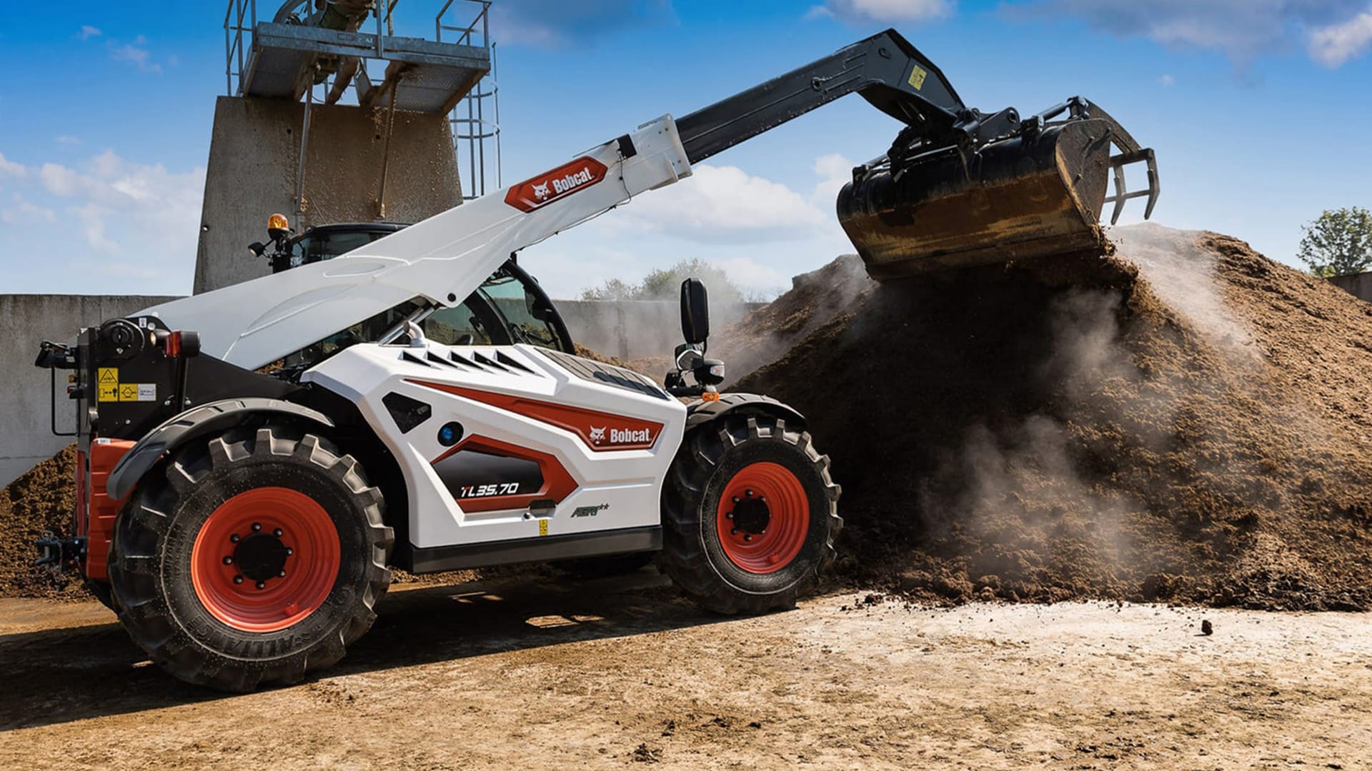 A Bobcat TL35.70 Agricultural Telehandler working in a feedlot, lifting and shifting a steaming pile of silage or compost with a grapple bucket attachment.