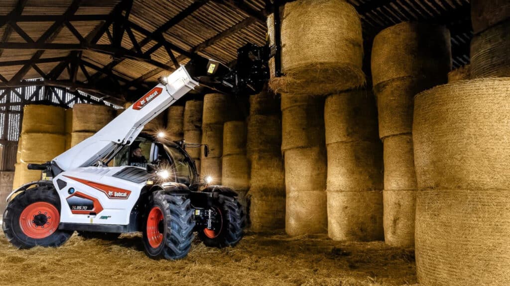 A Bobcat TL35.70 Agricultural Telehandler stacking large round hay bales inside a shed, showcasing its lifting height and precision handling in a farm setting.