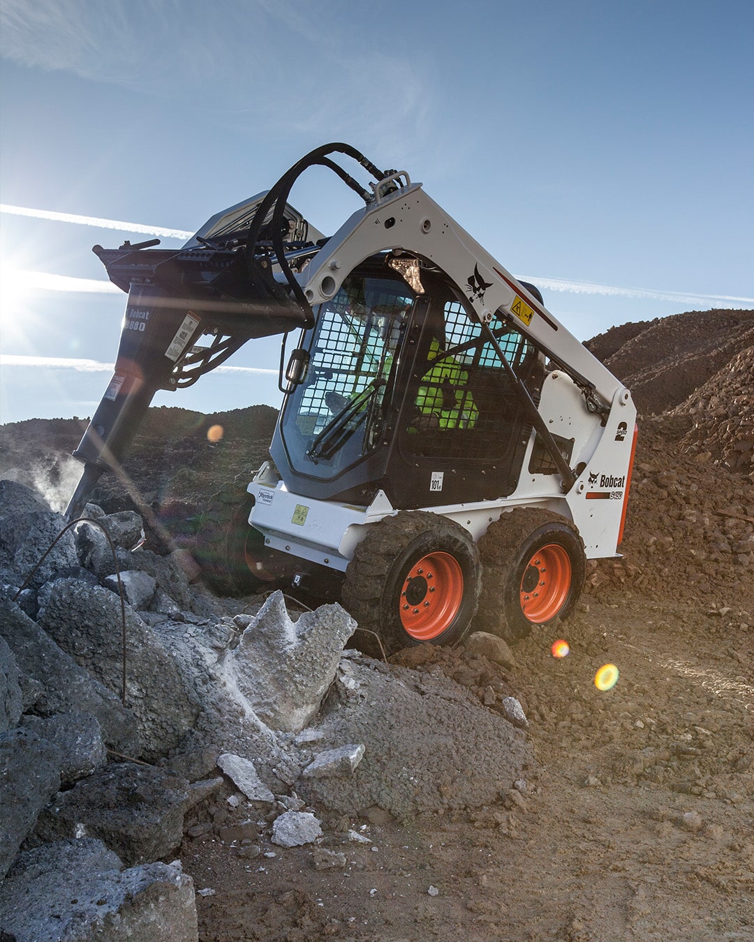 Bobcat S450 Skid Steer Loader using a hydraulic breaker to demolish concrete debris at a rugged construction site.