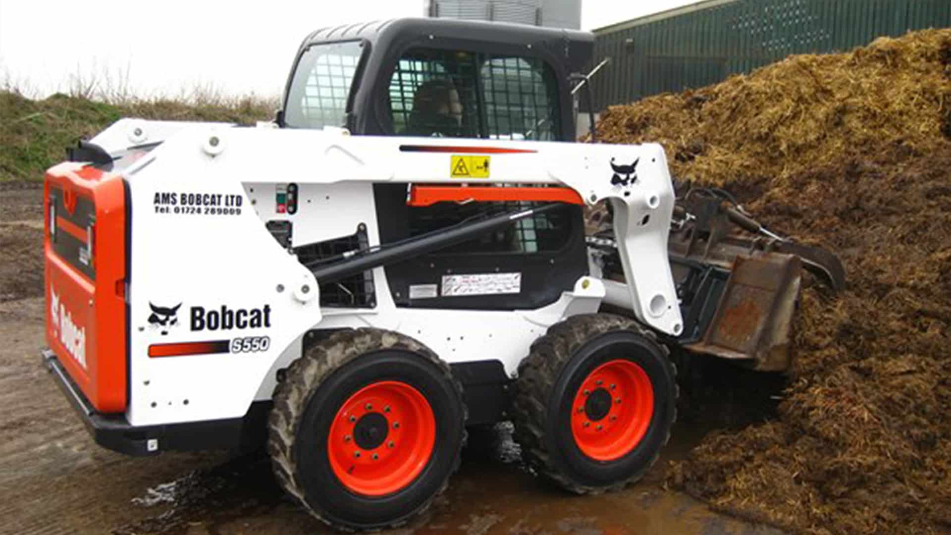 Bobcat S550 Skid Steer Loader handling a manure pile with a bucket attachment at an agricultural site.