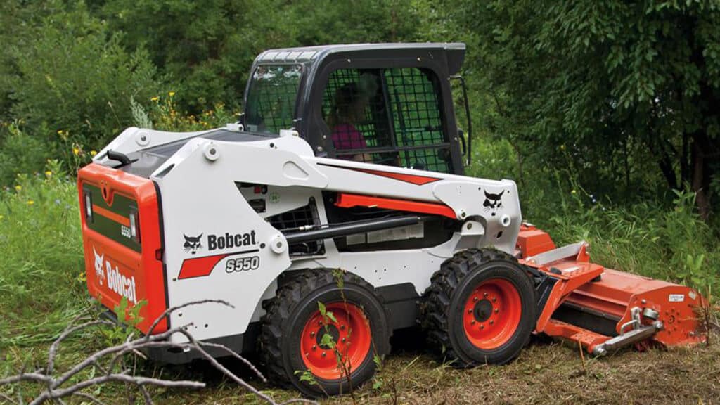 Bobcat S550 Skid Steer Loader equipped with a flail mower attachment, clearing dense vegetation in a rugged outdoor environment.