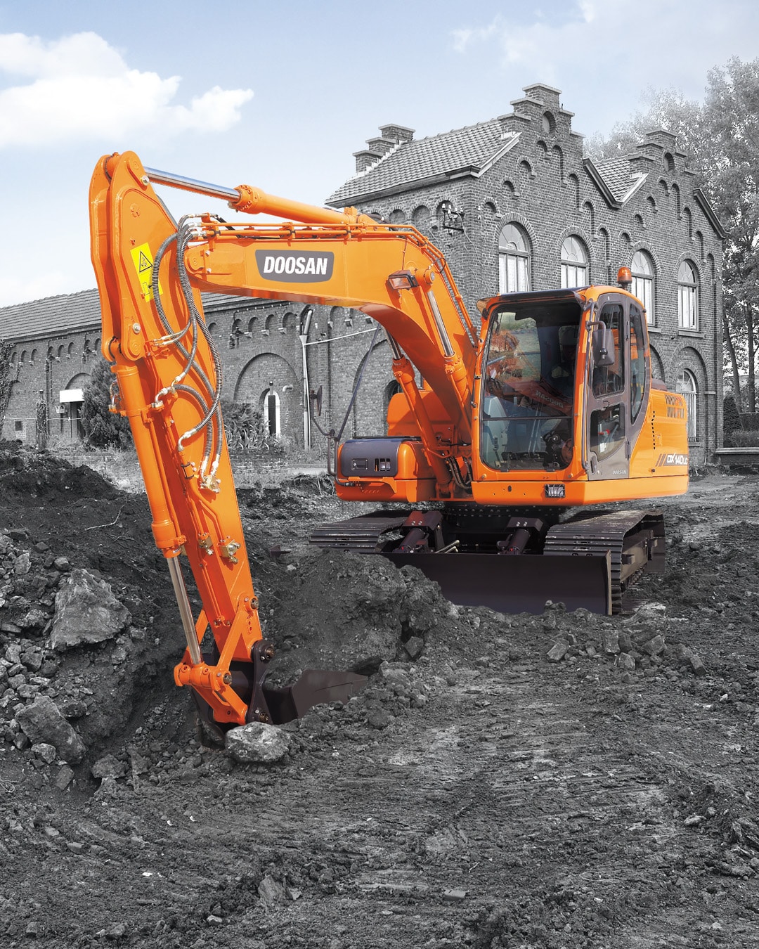 The vibrant orange Develon DX140LC Large Excavator digging into a rugged construction site with a powerful bucket. The excavator stands out in vivid colour against a grayscale background of the historic brick building and scattered rubble, emphasising its modern engineering and robust performance. The large windows of the cab provide excellent visibility, while the rubber tracks offer stability on uneven terrain. The contrasting colour scheme highlights the machine’s dominance in tough working conditions.