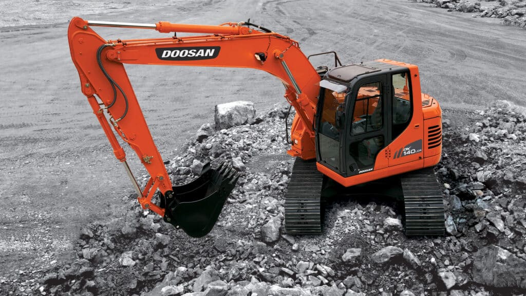 The vibrant orange Develon DX140LCR Large Excavator working on a rugged rock and gravel site. The excavator's powerful arm and claw bucket are poised for excavation, showcasing its strength and precision in tough environments. The durable rubber tracks provide stability on uneven, rocky terrain, while the spacious enclosed cabin ensures operator comfort and safety. The monochrome background emphasises the excavator’s bold colour, highlighting its modern and robust design amid the harsh landscape.
