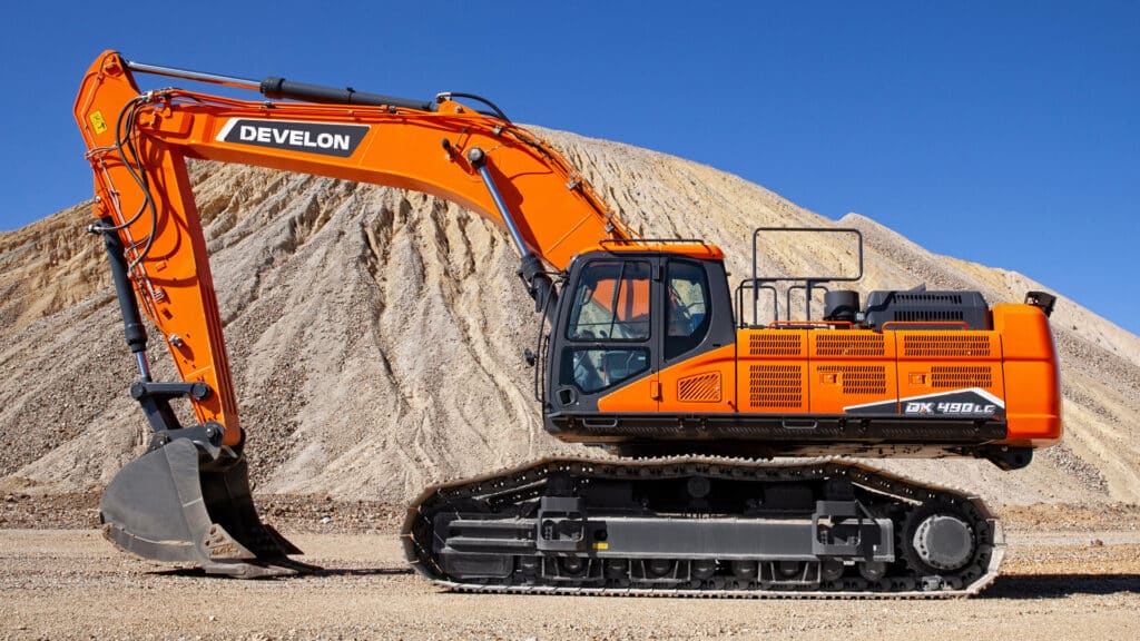 The Develon DX490LC-7M Large Excavator displayed against a backdrop of rugged gravel hills and clear blue skies. The machine’s bright orange body and powerful hydraulic arm emphasise its robust design and heavy-duty capabilities, ideal for large-scale earthmoving and excavation tasks.