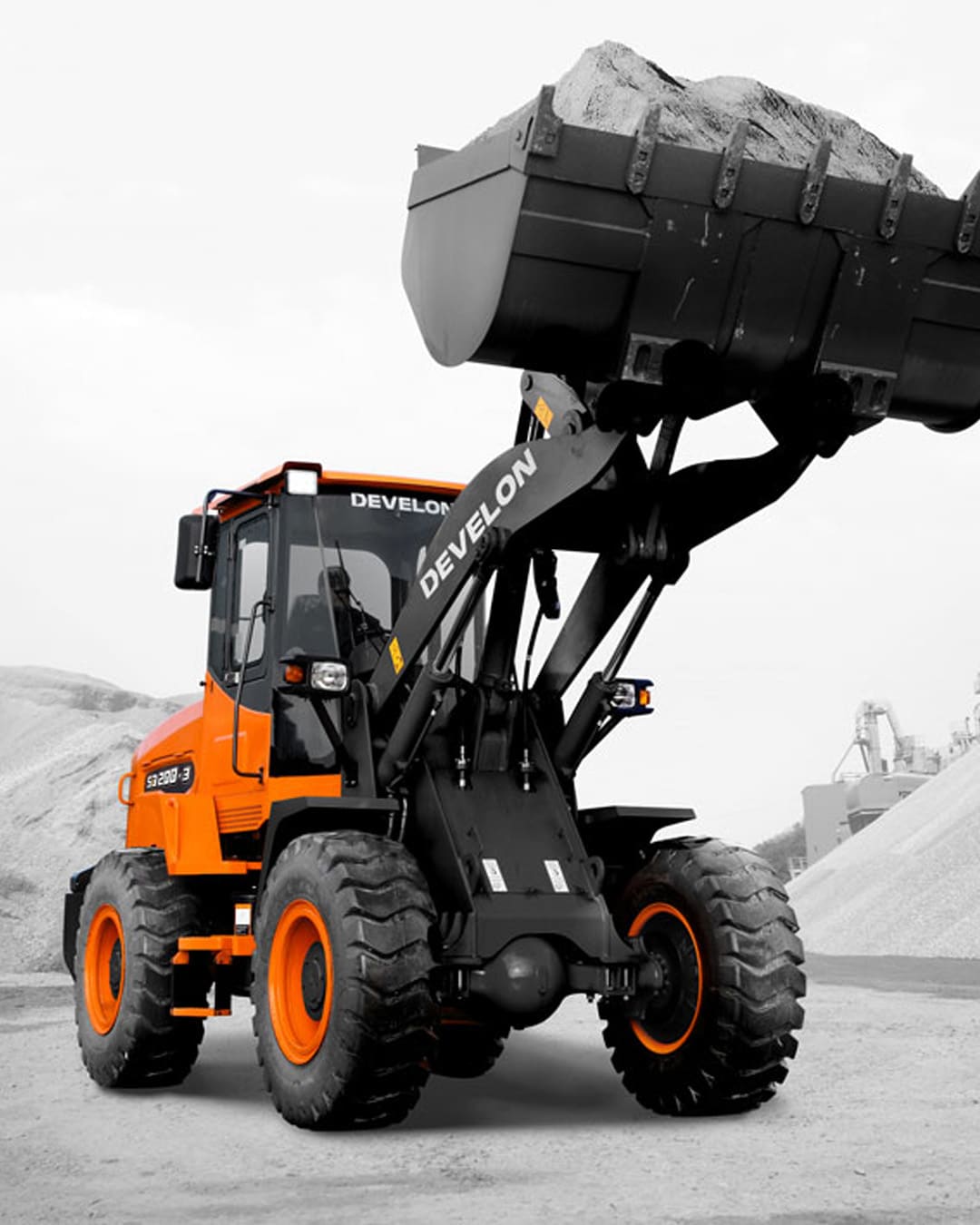 A Develon SD200 Wheel Loader lifting a full bucket of gravel on a rugged job site, showcasing its strength, durability, and efficient material handling capabilities.
