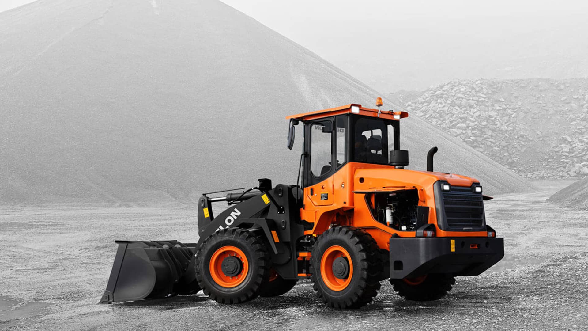 A Develon SD200 Wheel Loader working in a vast gravel quarry, highlighting its durability and efficiency in large-scale material handling and mining applications.