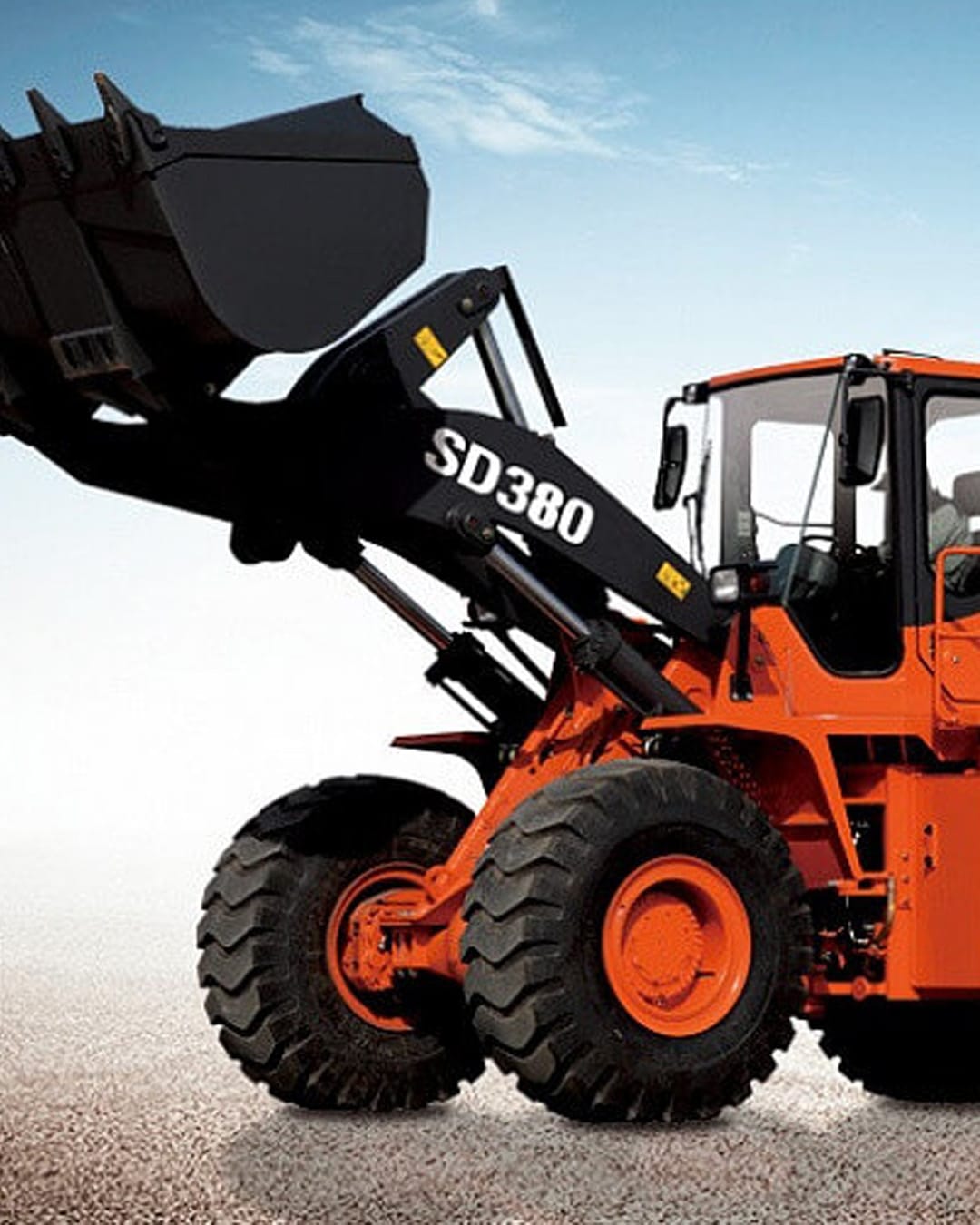 A Develon SD380 Wheel Loader with its bucket raised, showcasing its durable build and lifting power on a clear day.