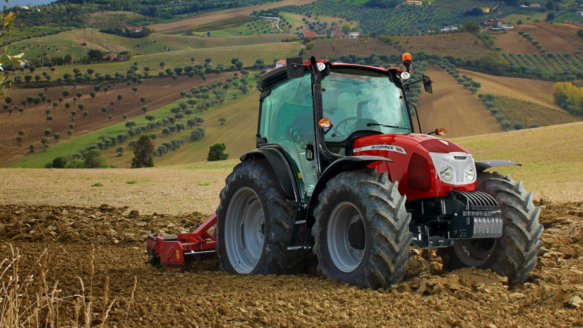 McCormick Farm Tractor tilling soil on a rolling hillside with a scenic agricultural landscape in the background.