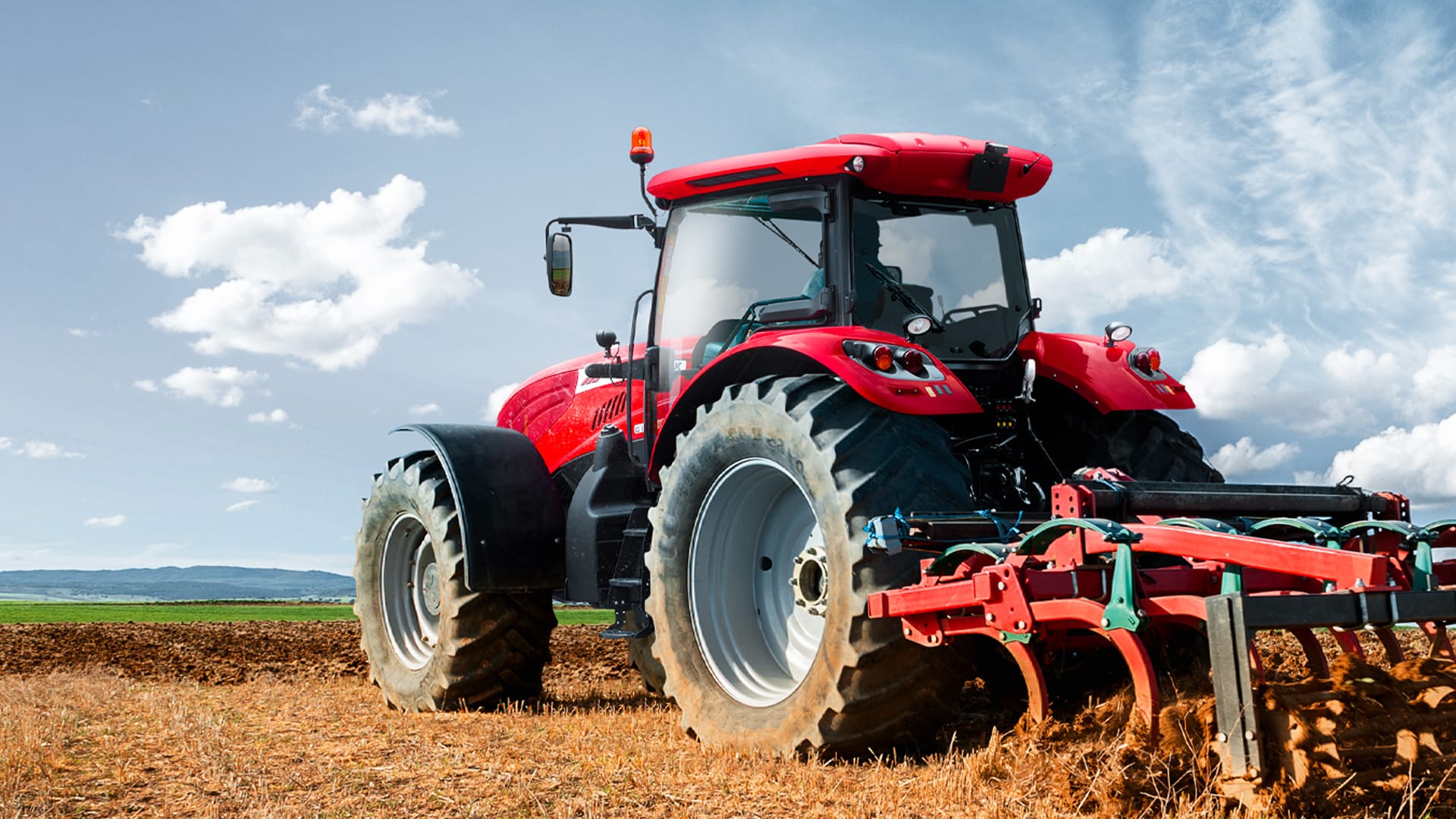 McCormick tractor cultivating a dry paddock under a bright blue sky.