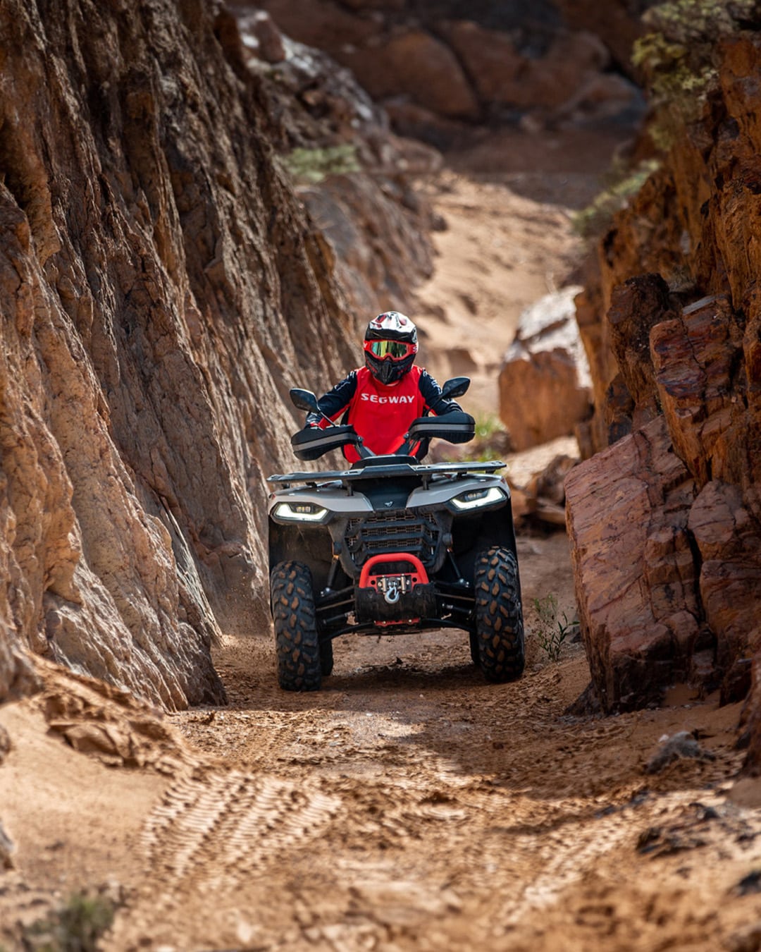 A rider wearing red Segway gear navigates a narrow, rocky canyon trail on a Segway AT5 S Farm Quad Bike, showcasing the quad bike’s agility and rugged performance in challenging off-road terrain.