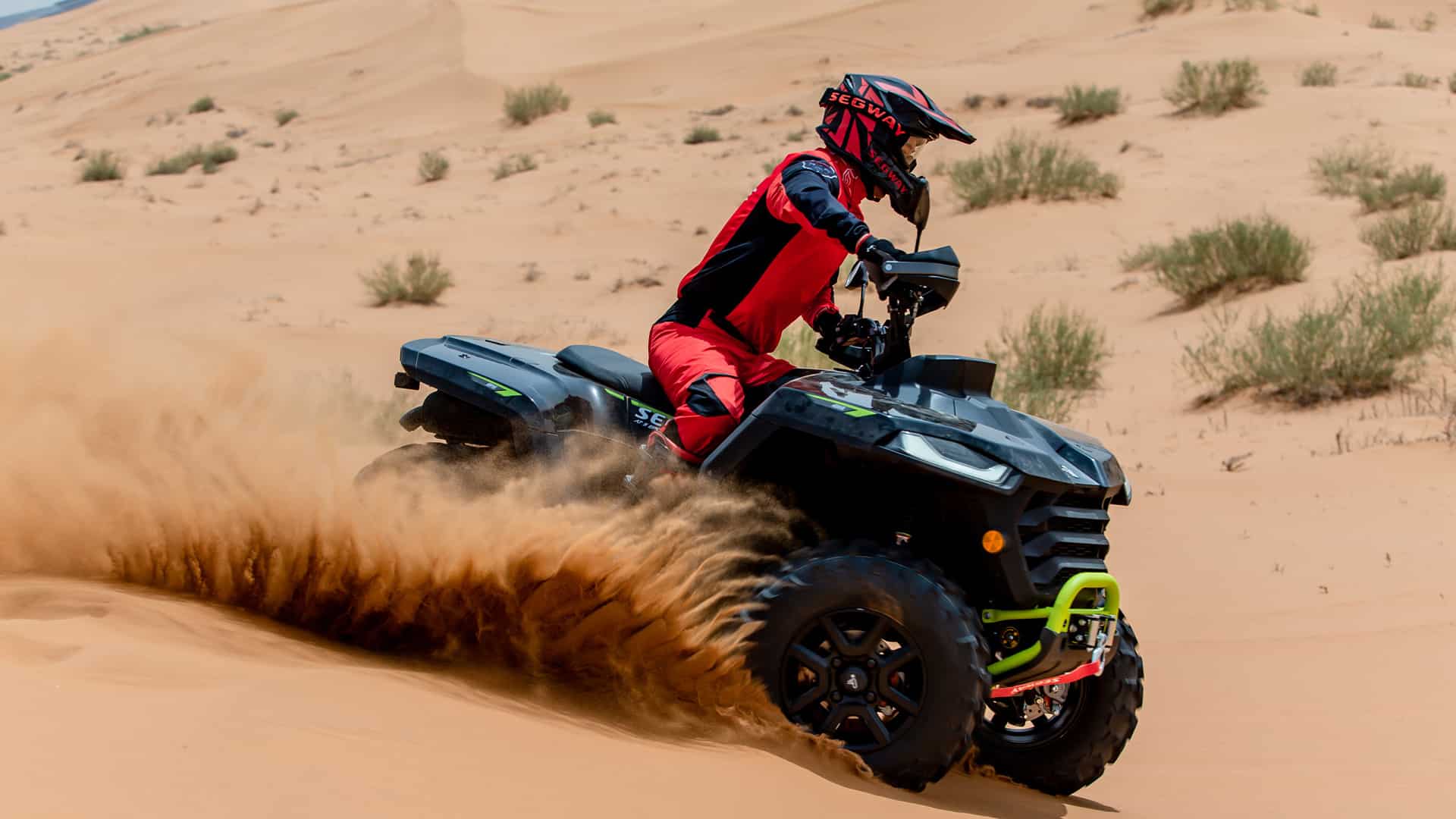 A rider in red Segway gear carves through soft desert sand on a Segway AT5 S Farm Quad Bike, kicking up a spray of dust to showcase its high-performance handling in extreme off-road conditions.
