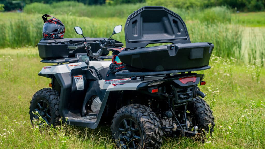 A Segway AT5 S Farm Quad Bike parked in a grassy field with an open rear storage box, helmet, and goggles resting on top, showcasing its practicality and storage capabilities for rural and farming tasks.