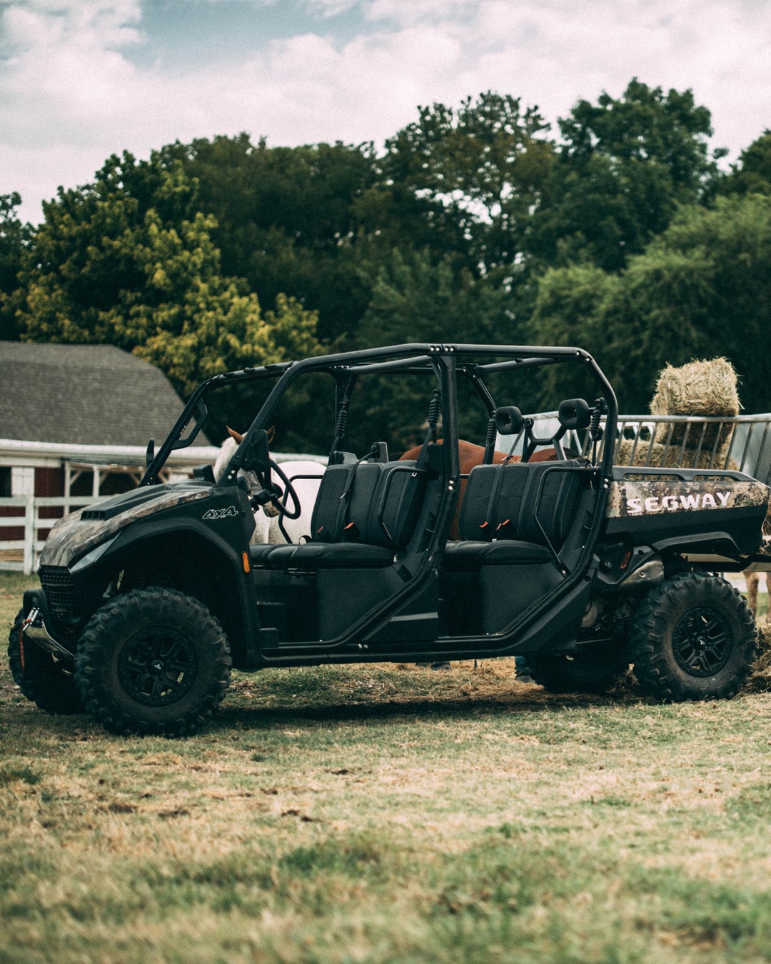 A Segway UT10 Crew Premium UTV is parked on a grassy farm property with hay bales loaded in the back, highlighting its spacious seating and utility for rural work.