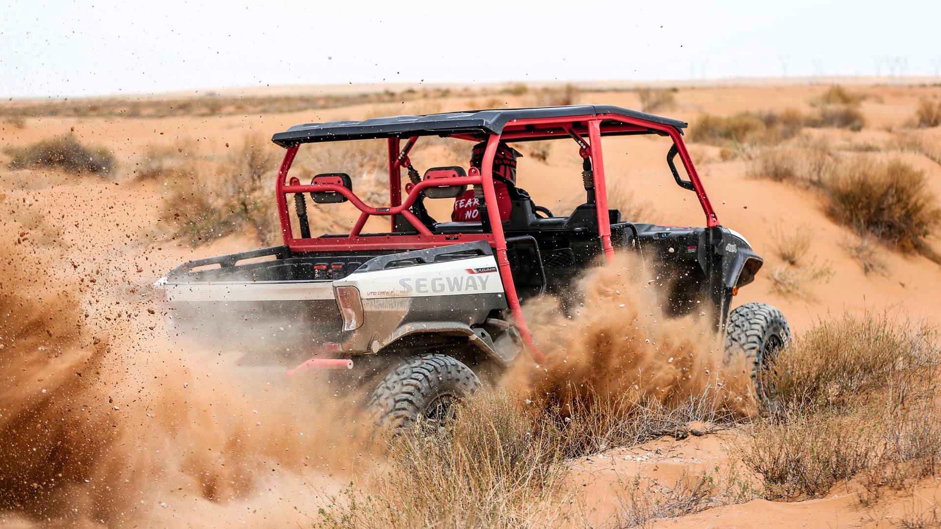 A Segway UT10 Crew Premium UTV kicks up sand as it powers through a desert trail, showcasing its off-road performance and rugged suspension in action.