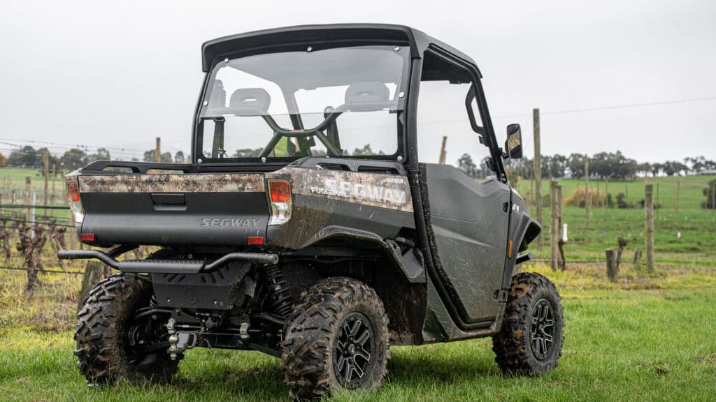 A Segway UT10 Navigator UTV with a camo rear panel and mud-covered tires is parked on a grassy farm, highlighting its rugged design and off-road capability.
