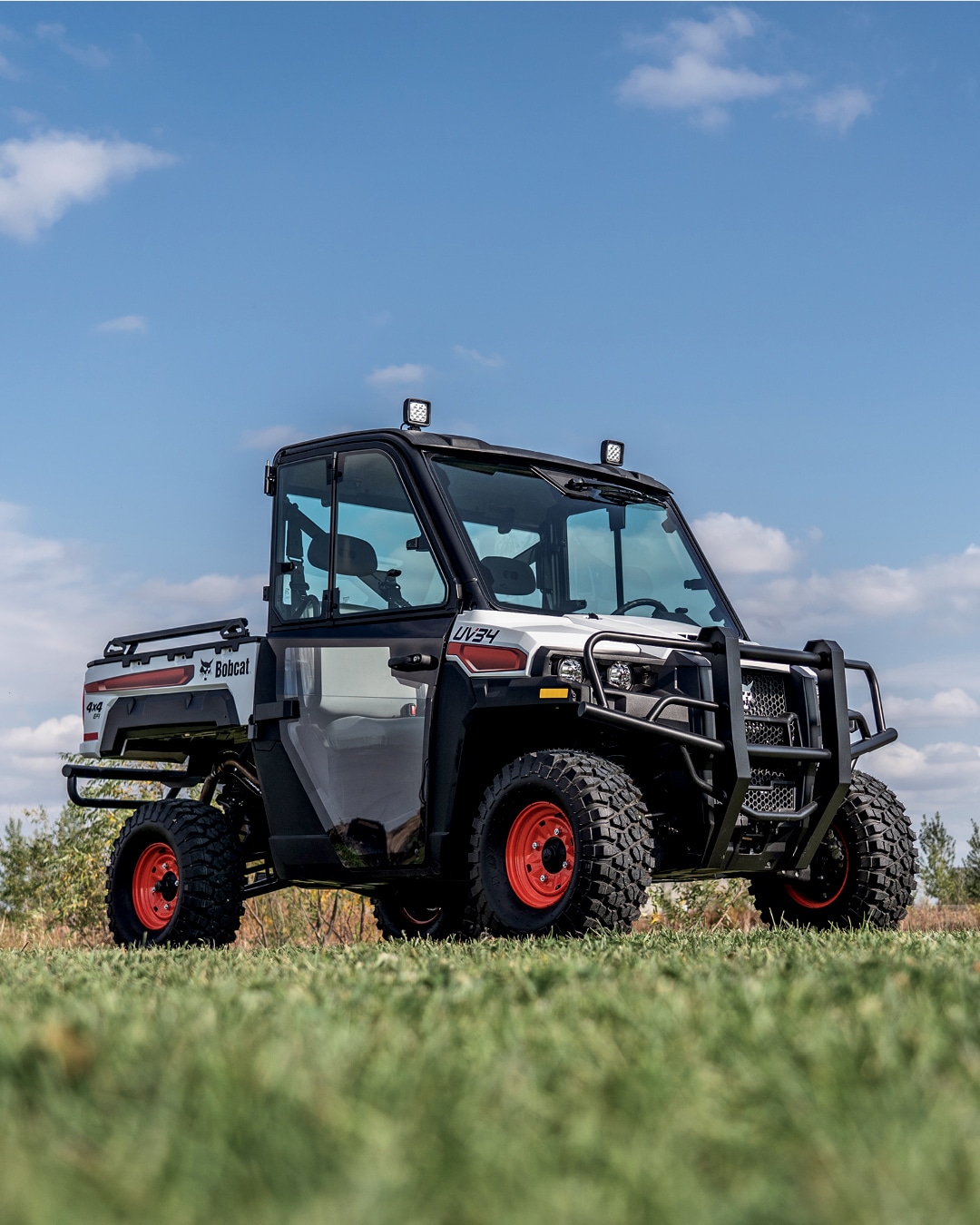 A Bobcat UTV with an enclosed cab and rugged tyres is parked on a grassy field under a blue sky, highlighting its durability and readiness for heavy-duty outdoor work.