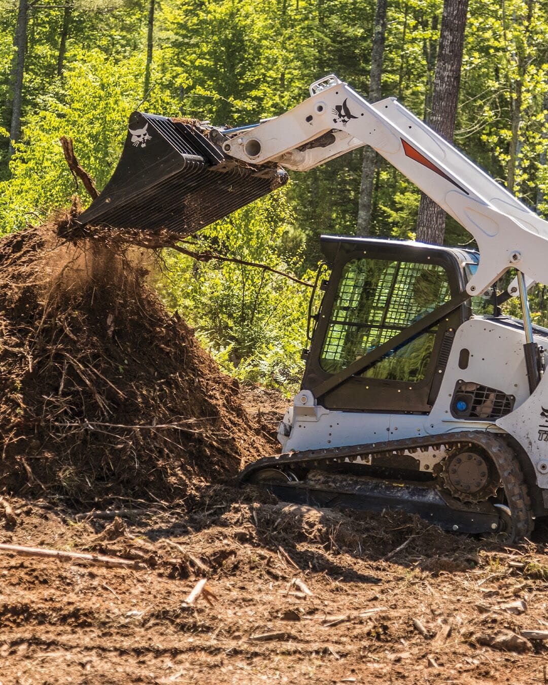 A Bobcat Track Loader lifting a pile of roots and debris with a skeleton bucket, showcasing its power and versatility in land clearing applications.